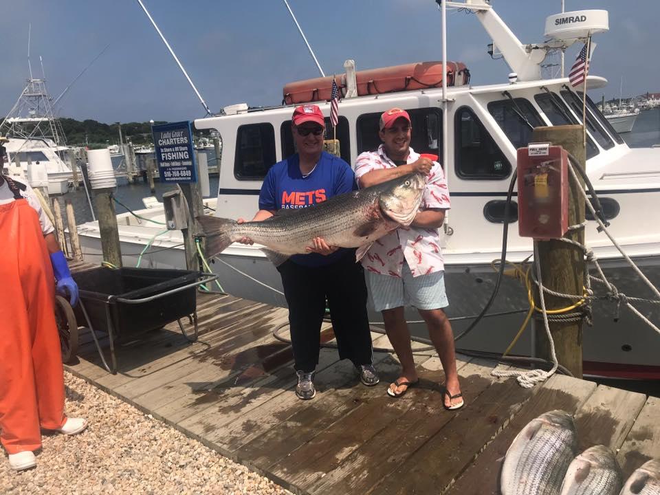 Guests holding a striped bass at the dock beside the charter boat